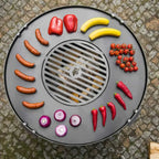 Barbecue portable à design noir et argent, doté de plusieurs compartiments pour cuire des saucisses, des poivrons, des oignons, des tomates, des bananes et d’autres aliments.