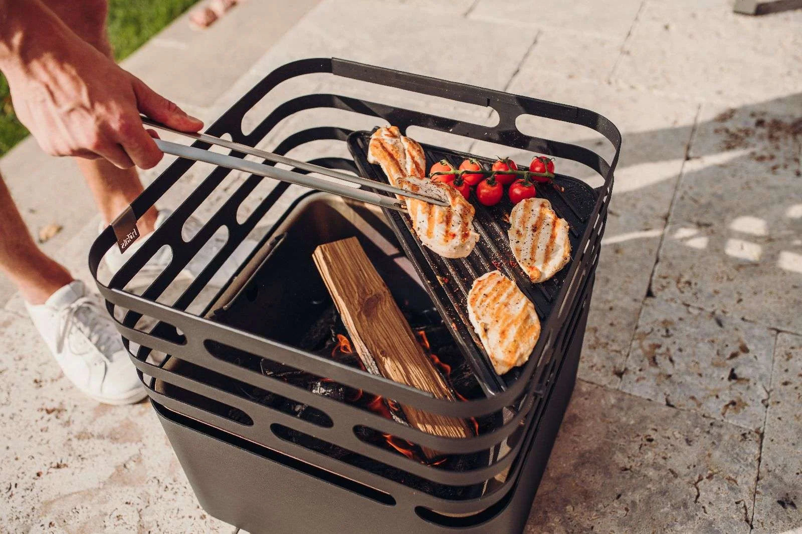 Barbecue au charbon avec cadre et couvercle en métal noir, bûches de bois pour combustible.