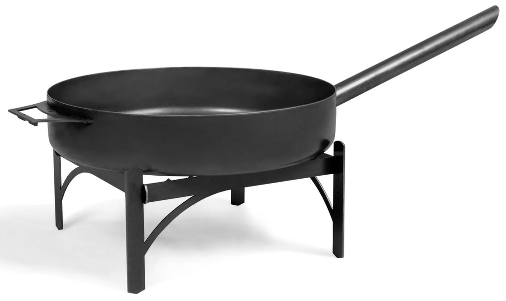 Poêle à paella en fonte noire sur support avec long manche et pieds courbés.