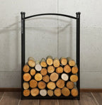 Porte-bûches en métal noir avec un haut courbé et des pointes sphériques, contenant des bûches empilées soigneusement dans diverses nuances de brun.