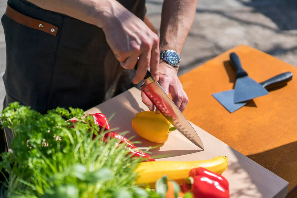 Un couteau de chef avec un manche noir et une lame en acier inoxydable dotée d’un bord dentelé, reposant sur une planche à découper orange.