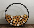 Support à bois circulaire noir avec des pieds en métal et des bûches en bois à l’intérieur.