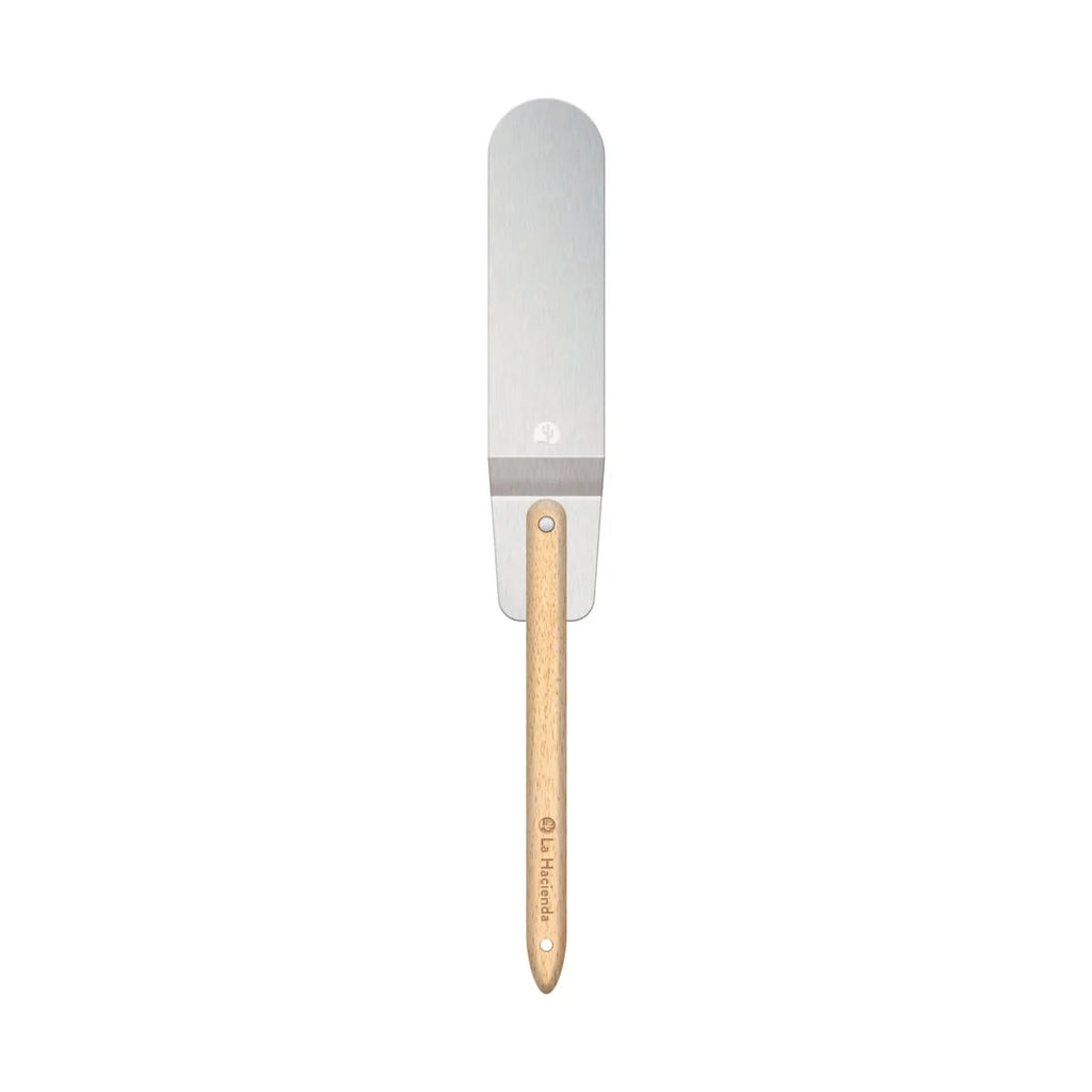 Une spatule en métal argenté élégante avec un manche en bois clair et le nom de marque « la hacienda » gravé dessus.