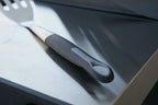 Spatule grise et blanche avec une poignée à prise texturée, probablement en silicone ou en caoutchouc.