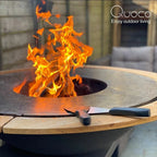 Foyer de feu extérieur Quoco avec une flamme orange vibrante et un couvercle en bois.