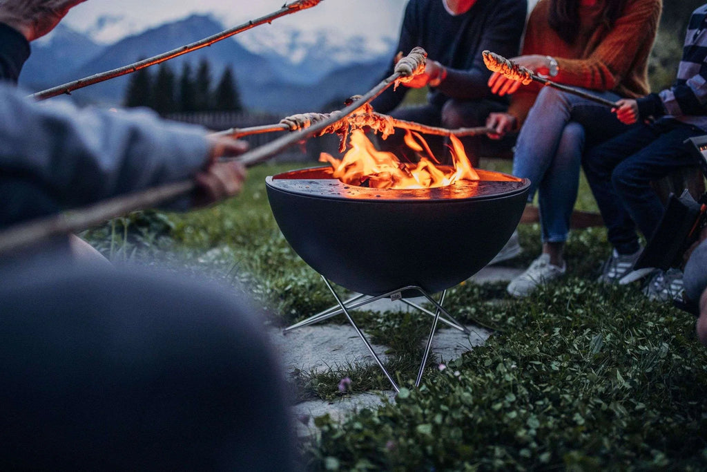 Fosse de feu en bol noir avec pieds et poignées en métal pour faire griller des guimauves.