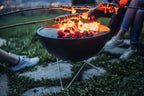 Gril barbecue rond noir avec des pieds en métal et du feu qui brûle à l’intérieur.