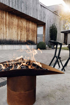 Foyer de feu en métal rouillé avec un design triangulaire et des pieds noirs.