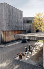 Maison en bois moderne avec toit courbé et terrasse en briques.