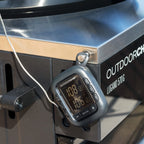 Thermomètre numérique argenté avec affichage noir et boutons, fixé sur une grille en acier inoxydable.
