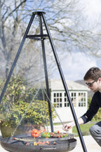 Barbecue suspendu noir de style trépied avec un bassin de cuisson rond rempli de feu et des suspensions par chaîne