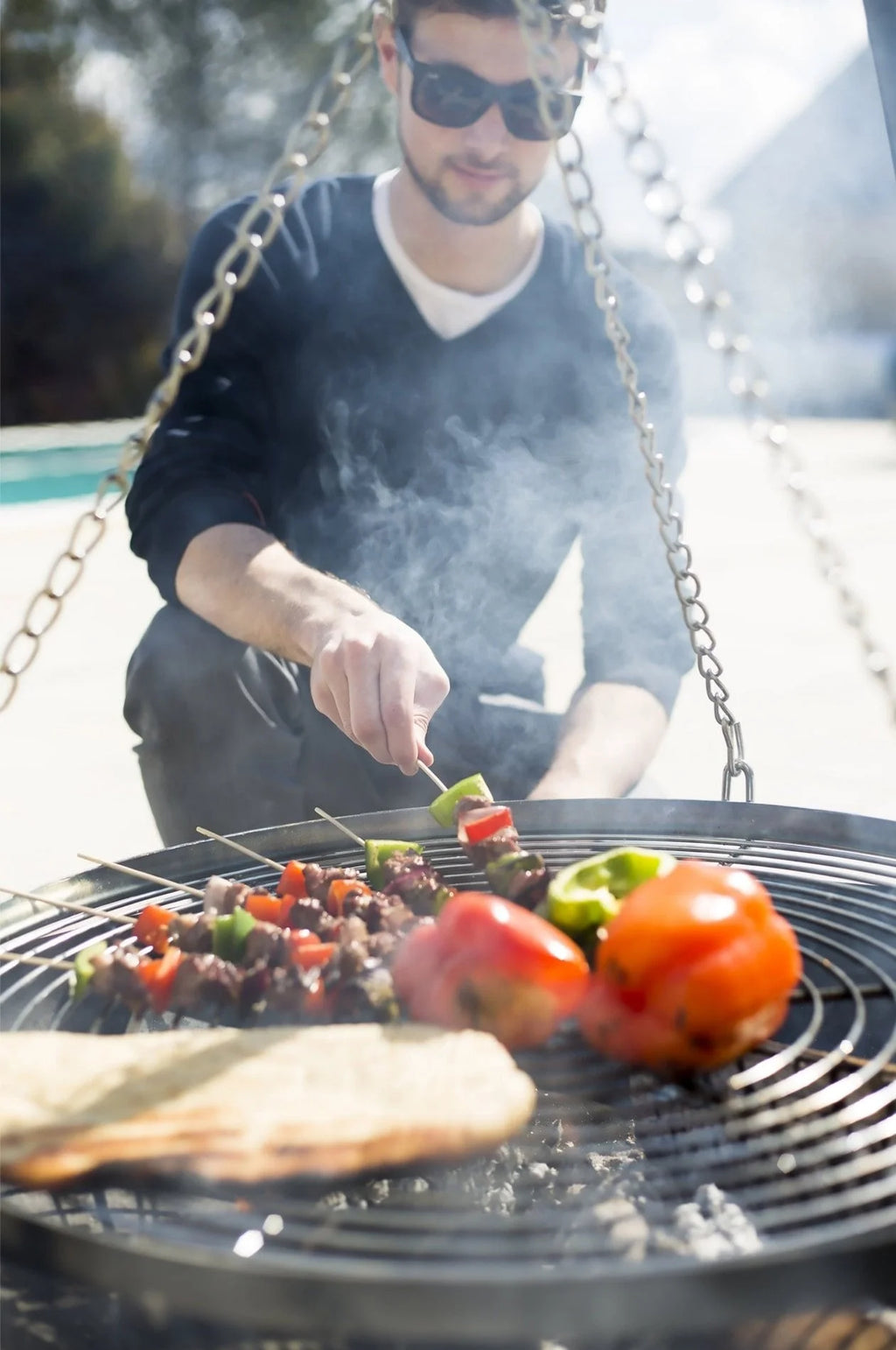 Barbecue au charbon rond noir avec grilles en métal et chaînes suspendues.