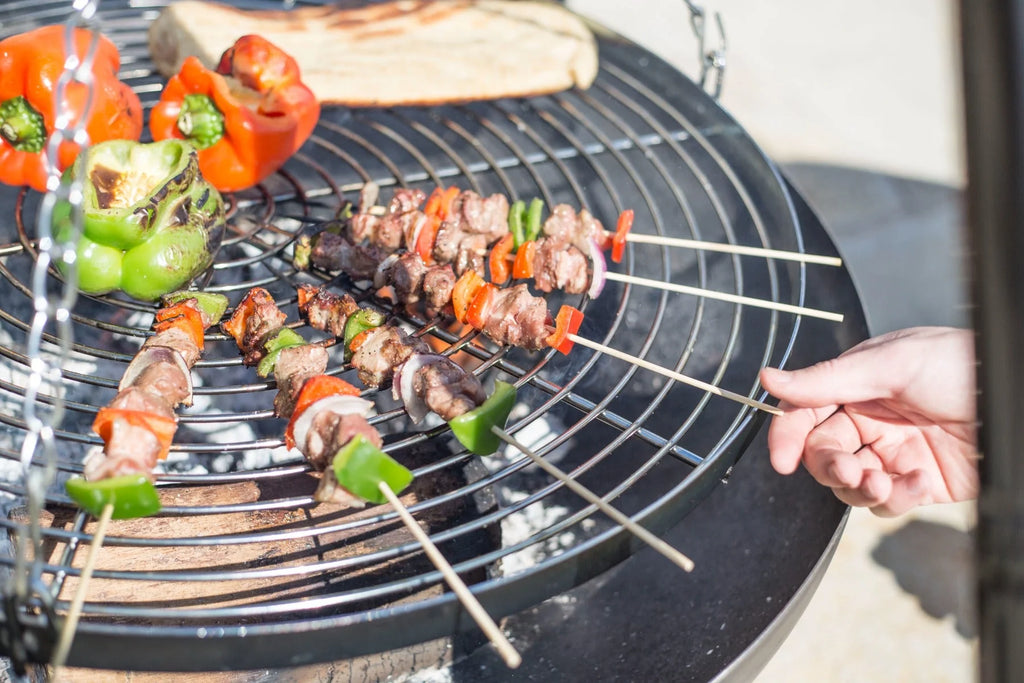 Brochettes en bois avec des morceaux de viande et des poivrons colorés alternés, grillées sur un barbecue au charbon.