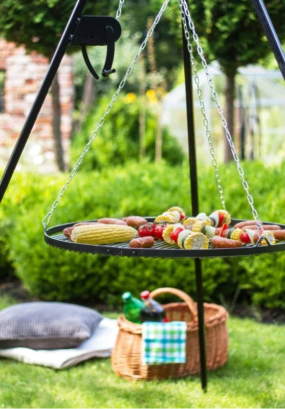 Gril suspendu avec cadre en métal noir et chaînes, contenant divers aliments grillés comme du maïs en épi.